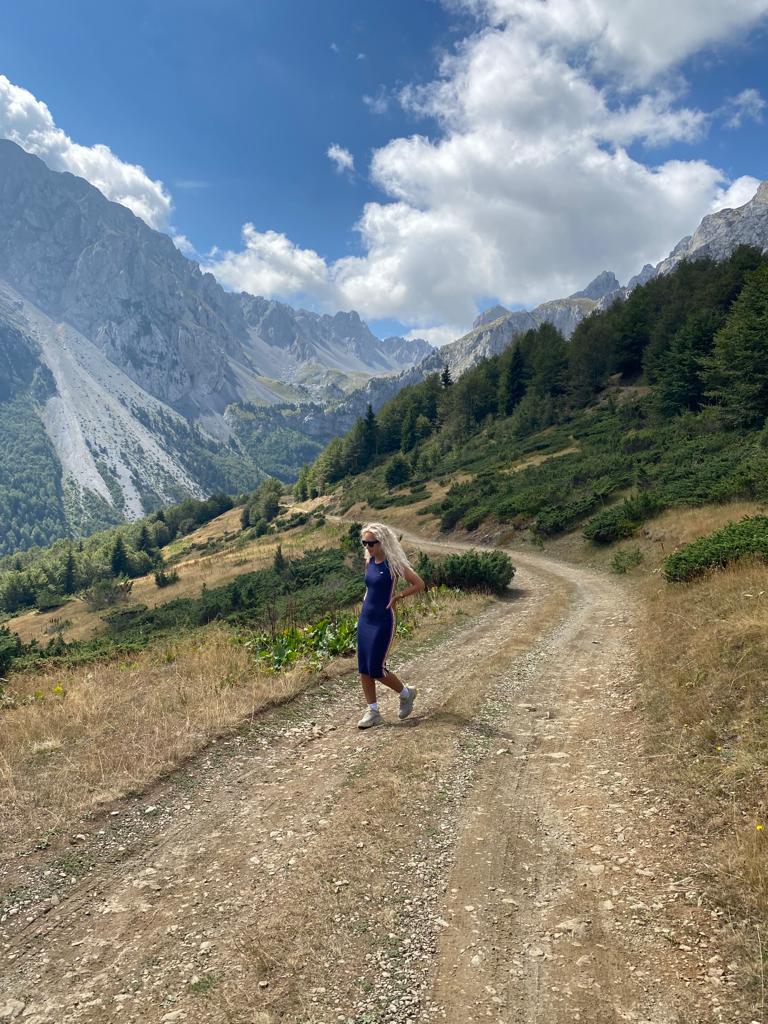 Plava kovrdžava devojka stoji na brdu, na zemljanom putu, okružena planinama. Komovi, Crna Gora